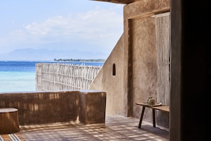 A balcony with a view of the sea, a wooden table, and a woven fence.