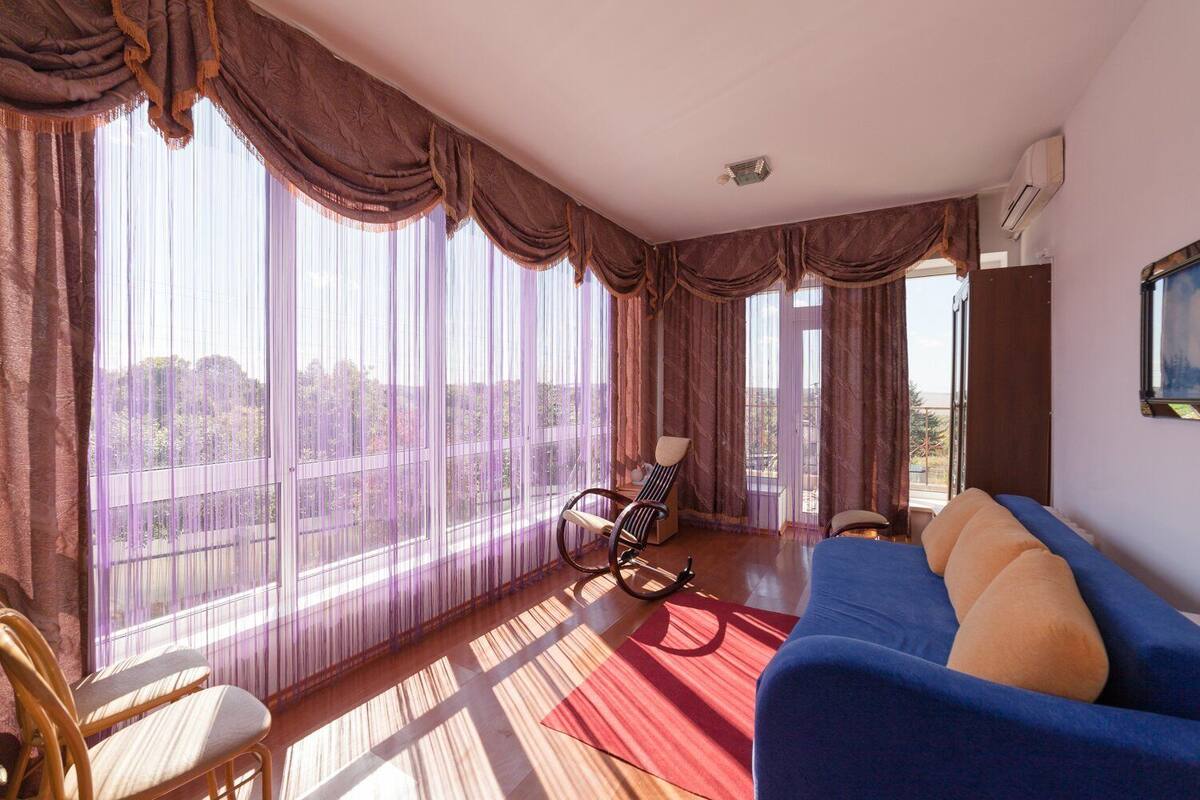Una habitación con un ventanal grande, un sofá azul, un sillón mecedor y una alfombra roja.