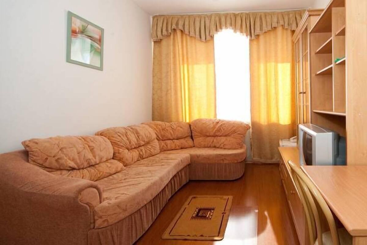 Una sala de estar con un amplio sofá en forma de L, una mesa de centro de madera y un televisor sobre un mueble.