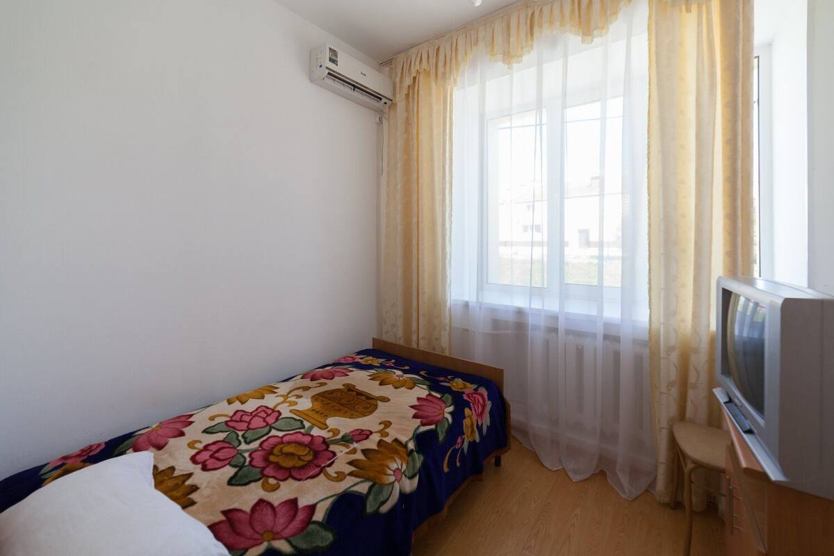 Una habitación pequeña y sencilla con una cama, un televisor y una ventana con cortinas.