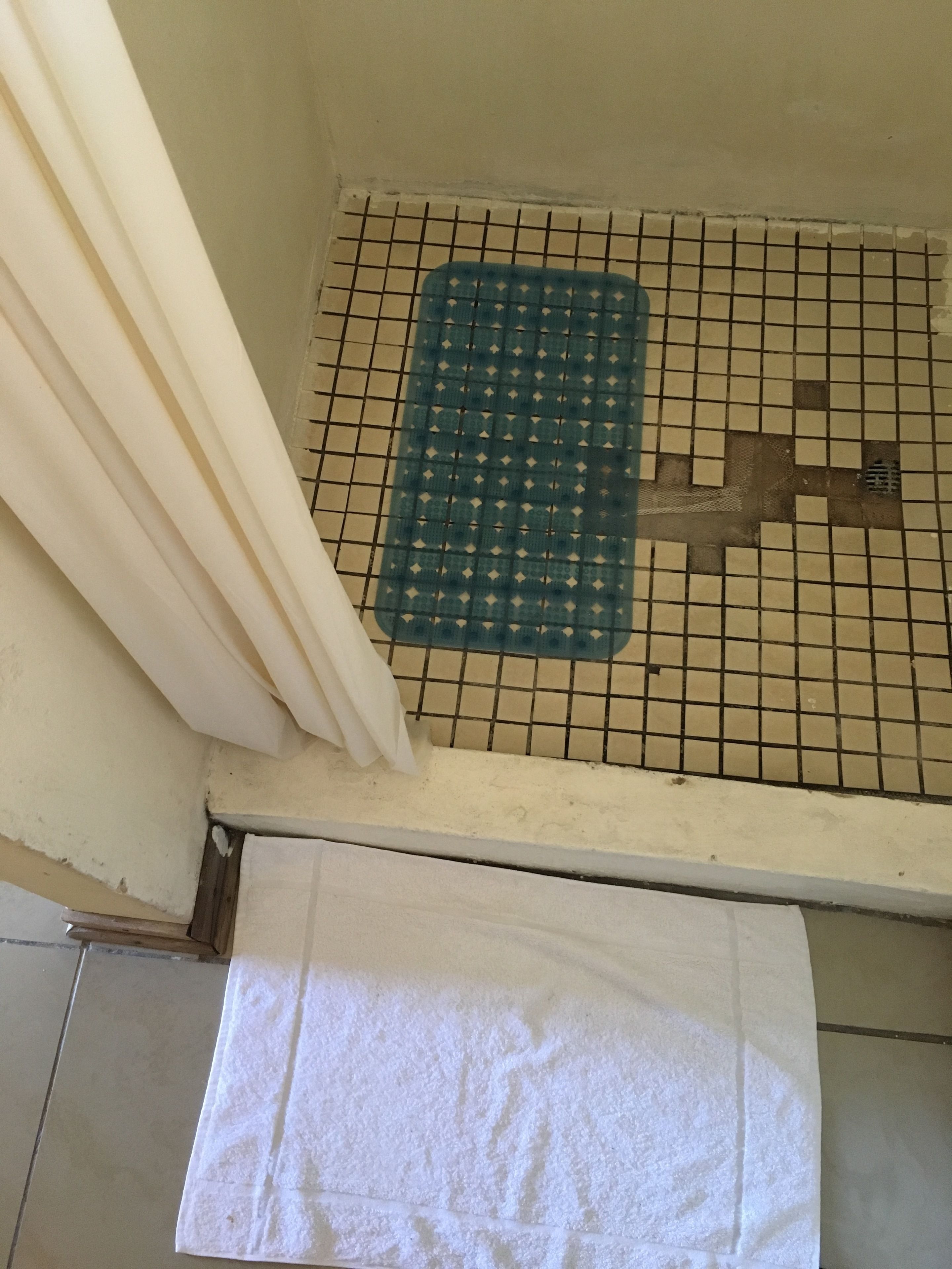 Un baño con piso de baldosas, zona de ducha y una toalla blanca en el suelo.