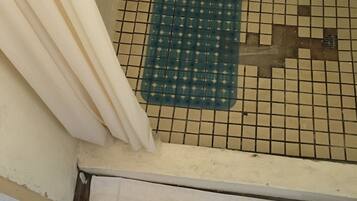 Un baño con piso de baldosas, zona de ducha y una toalla blanca en el suelo.