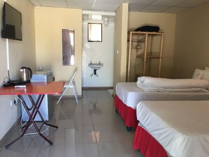 A hotel room with two beds, a desk with a kettle, a chair, a sink, and a wardrobe. - Athoma Guest House (Shakawe)