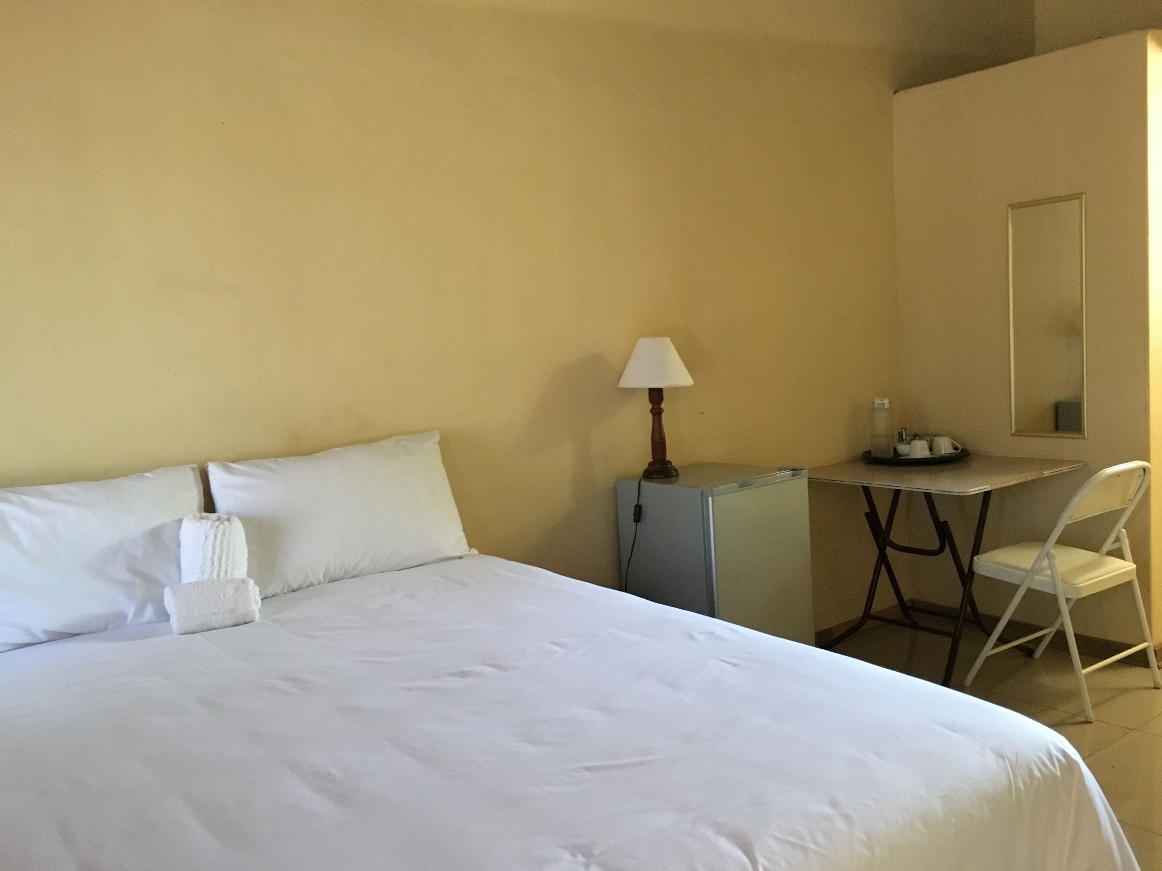 Una habitación de hotel con cama, escritorio, silla, lámpara y espejo.