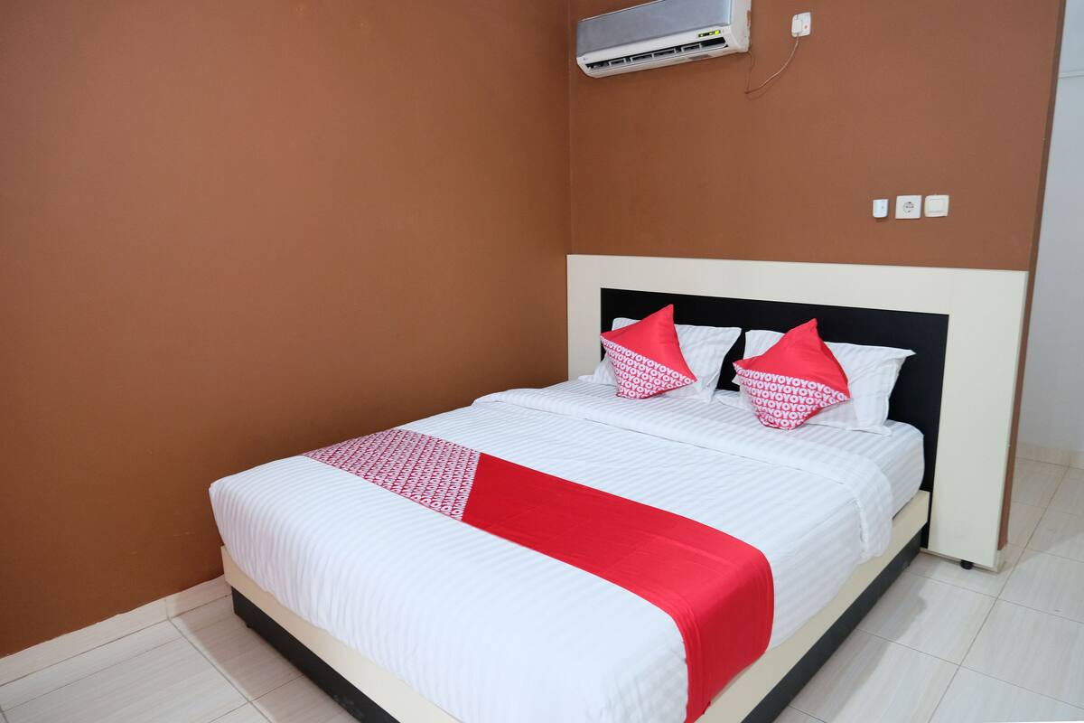 A neatly made bed with white and red bedding, a black headboard, and a red accent pillow.