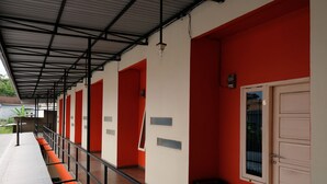 A covered outdoor area with a metal roof, red and white walls, and a series of doors. - Hotel O Mars Kost Syariah (Jambi)