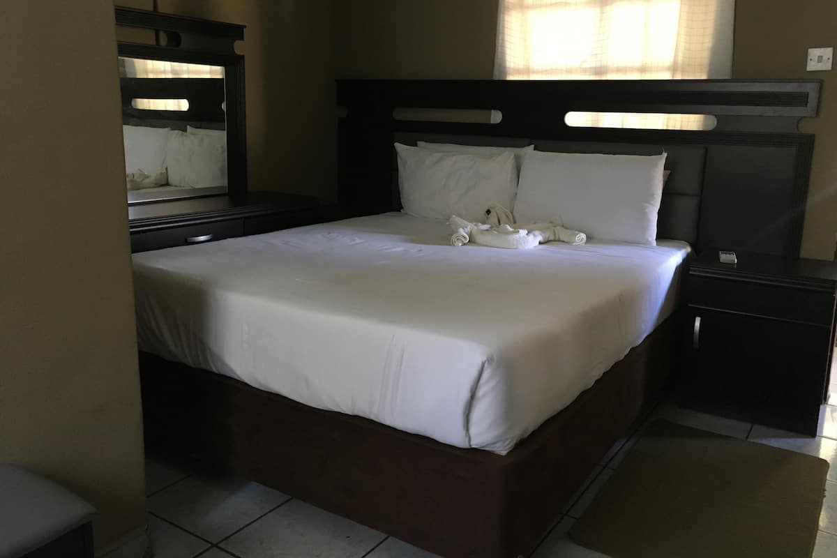 A neatly made bed with white linens, a dark headboard, and a bedside table with a lamp.