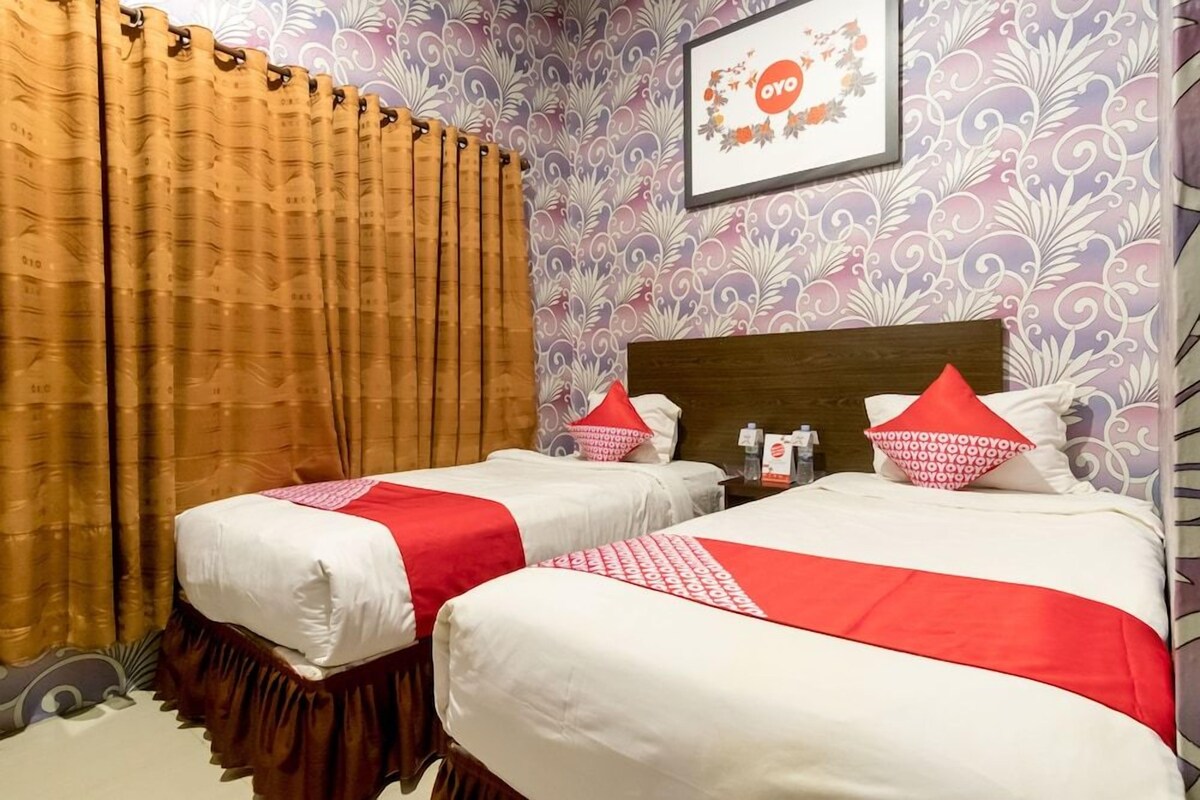 Een hotelkamer met twee bedden, een houten hoofdeinde en een wand met een bloemenmotief.