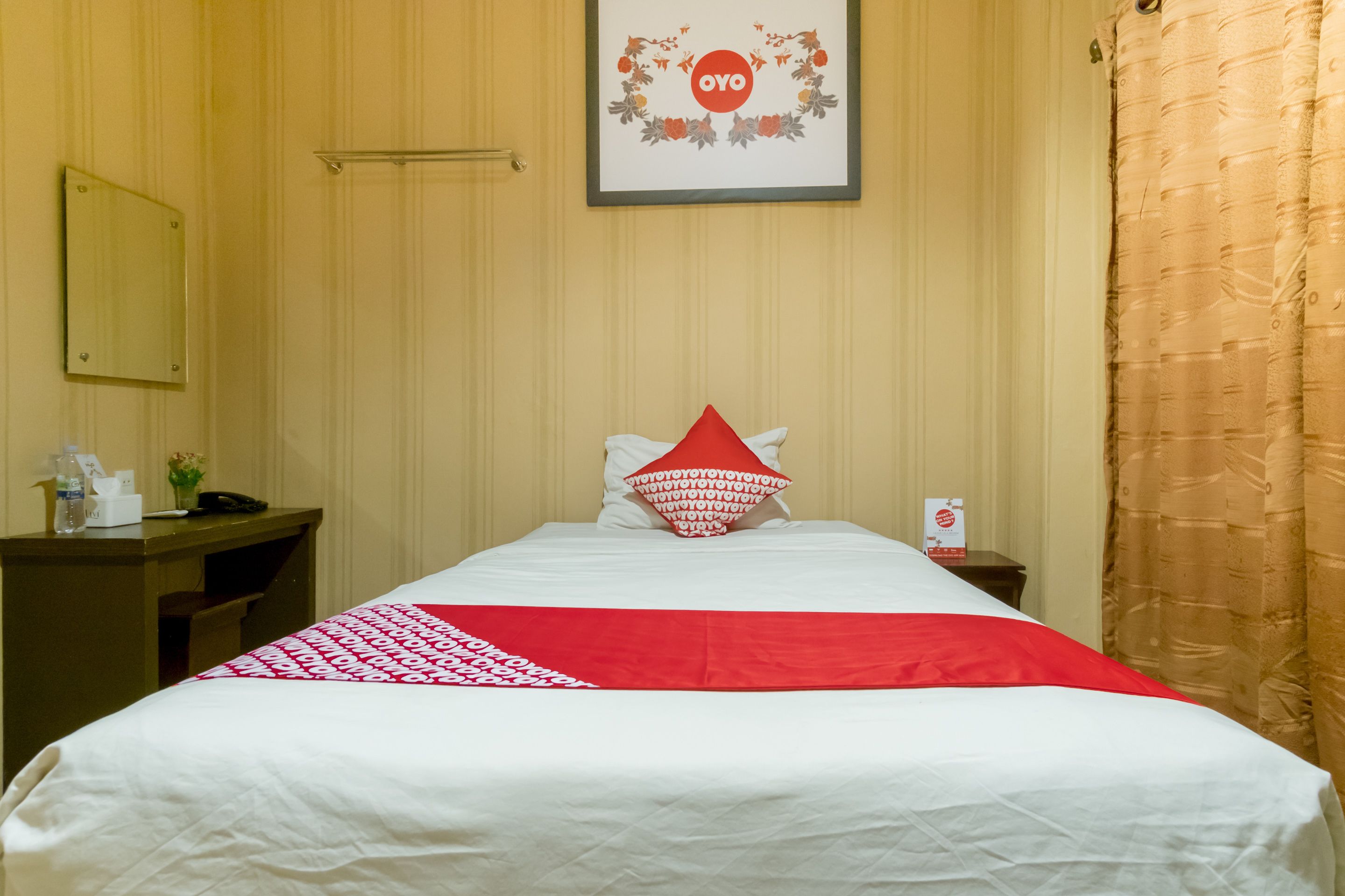 Une chambre d’hôtel avec un lit, un bureau, un téléphone, un tableau encadré au mur et un rideau.