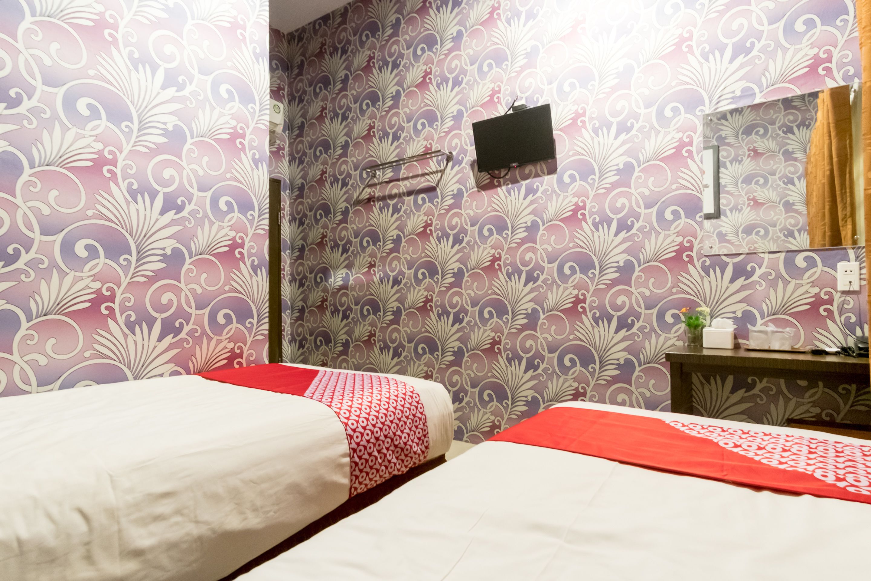 A hotel room with two beds, a TV mounted on the wall, and a mirror above a wooden dresser.