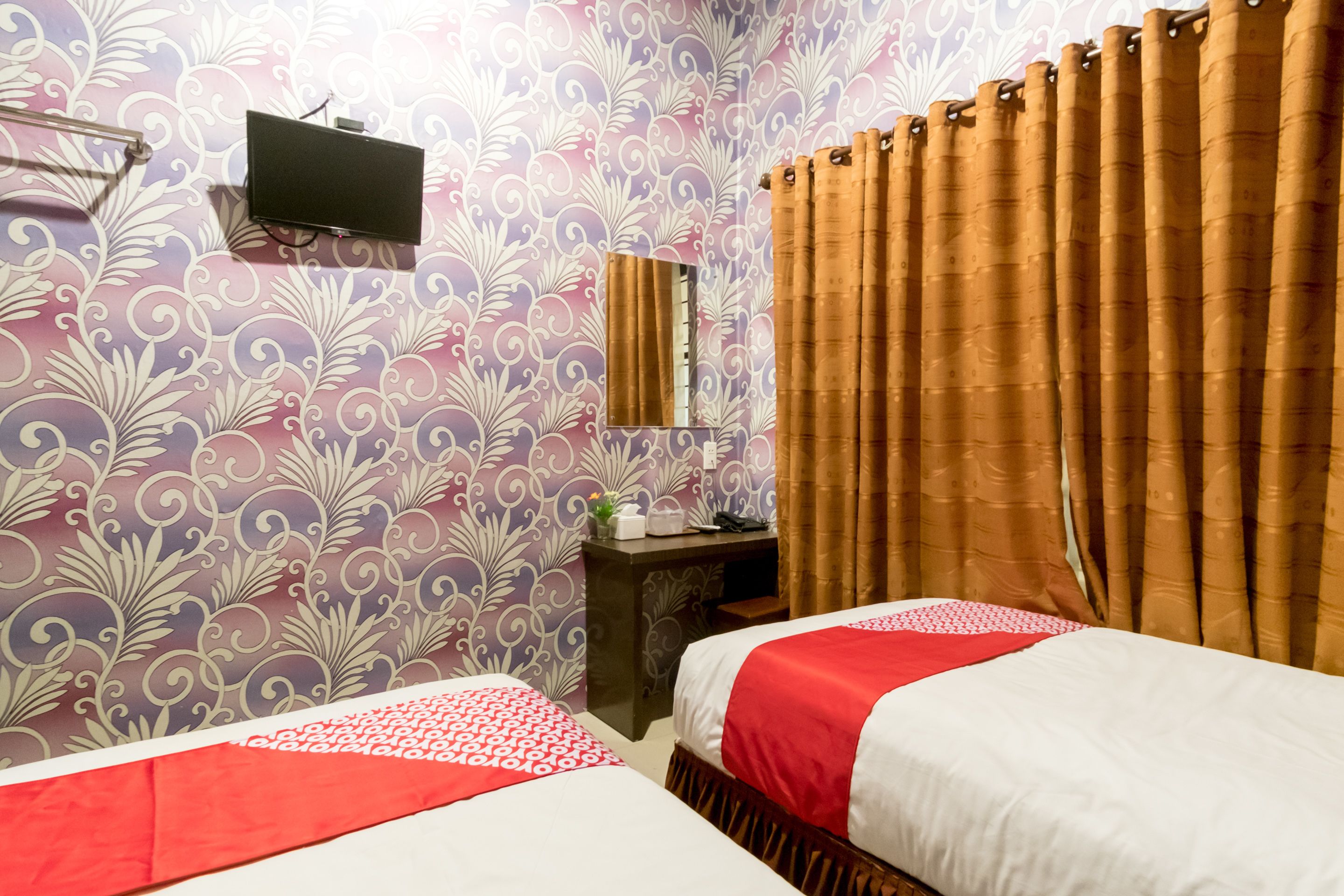 Hotellihuone, jossa on kaksi sänkyä, työpöytä, seinälle asennettu televisio ja verho.