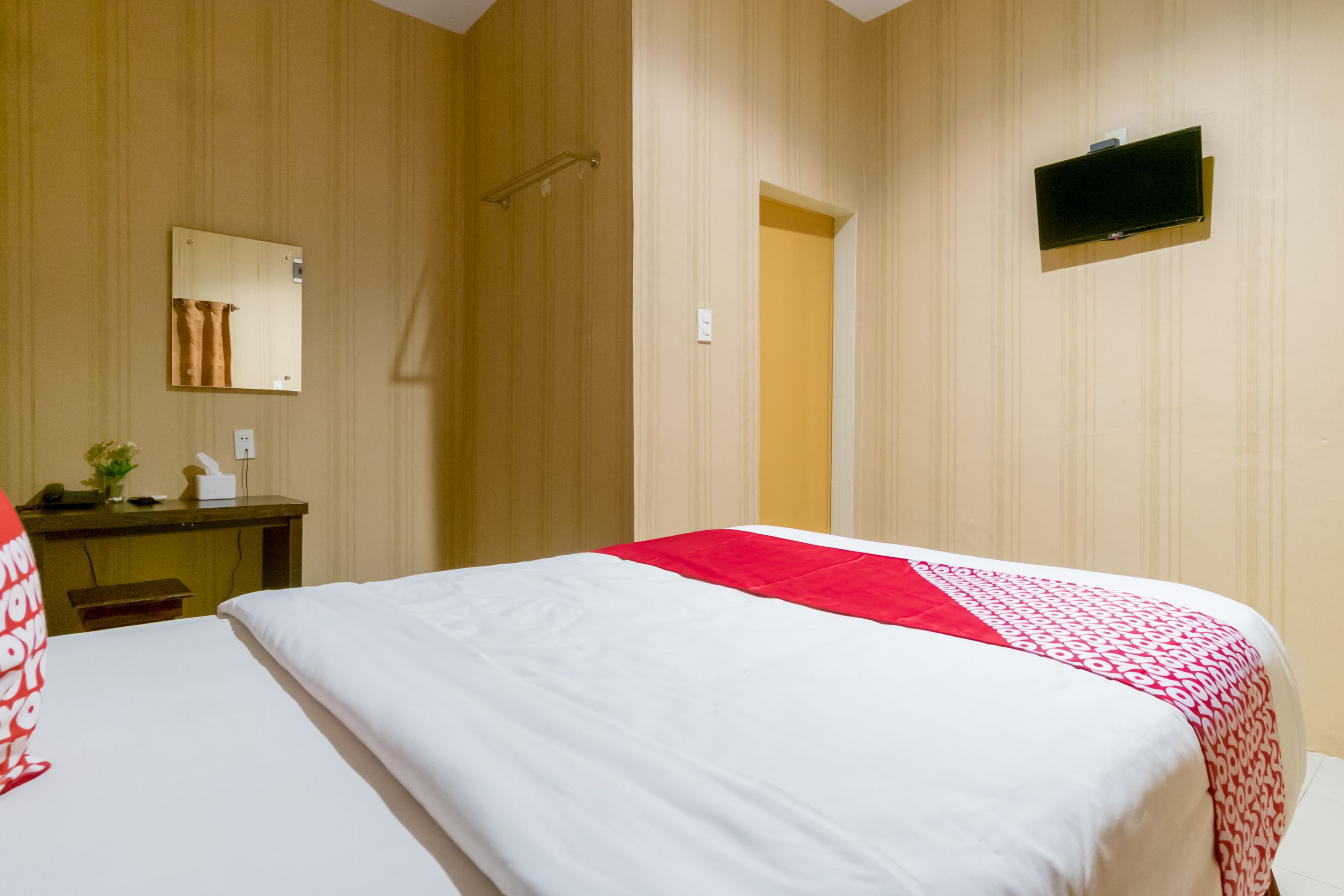 A hotel room with a bed, a desk, a mirror, and a television.