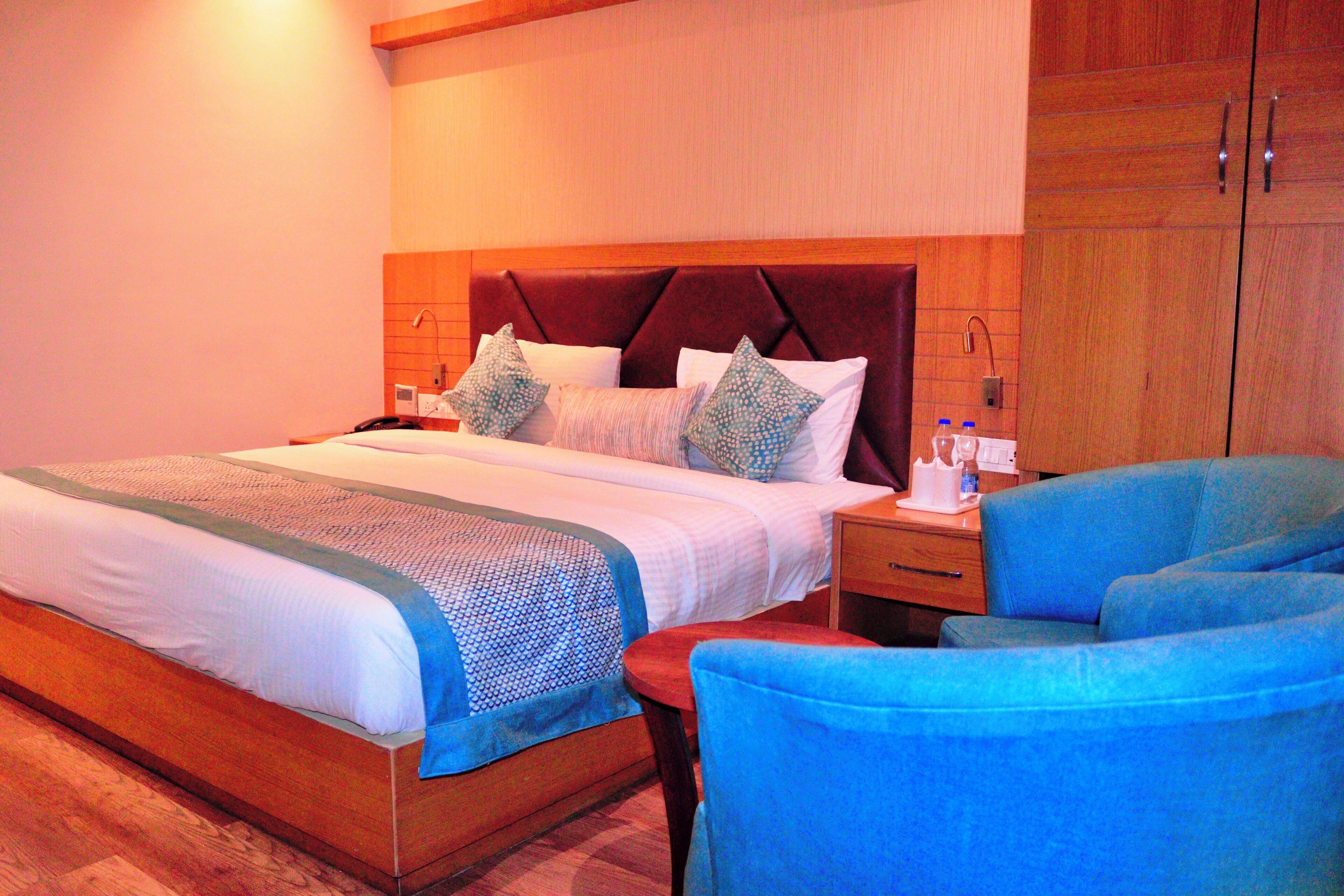 A hotel room with a large bed, a wooden headboard, a nightstand, a blue armchair, and a wooden wardrobe.