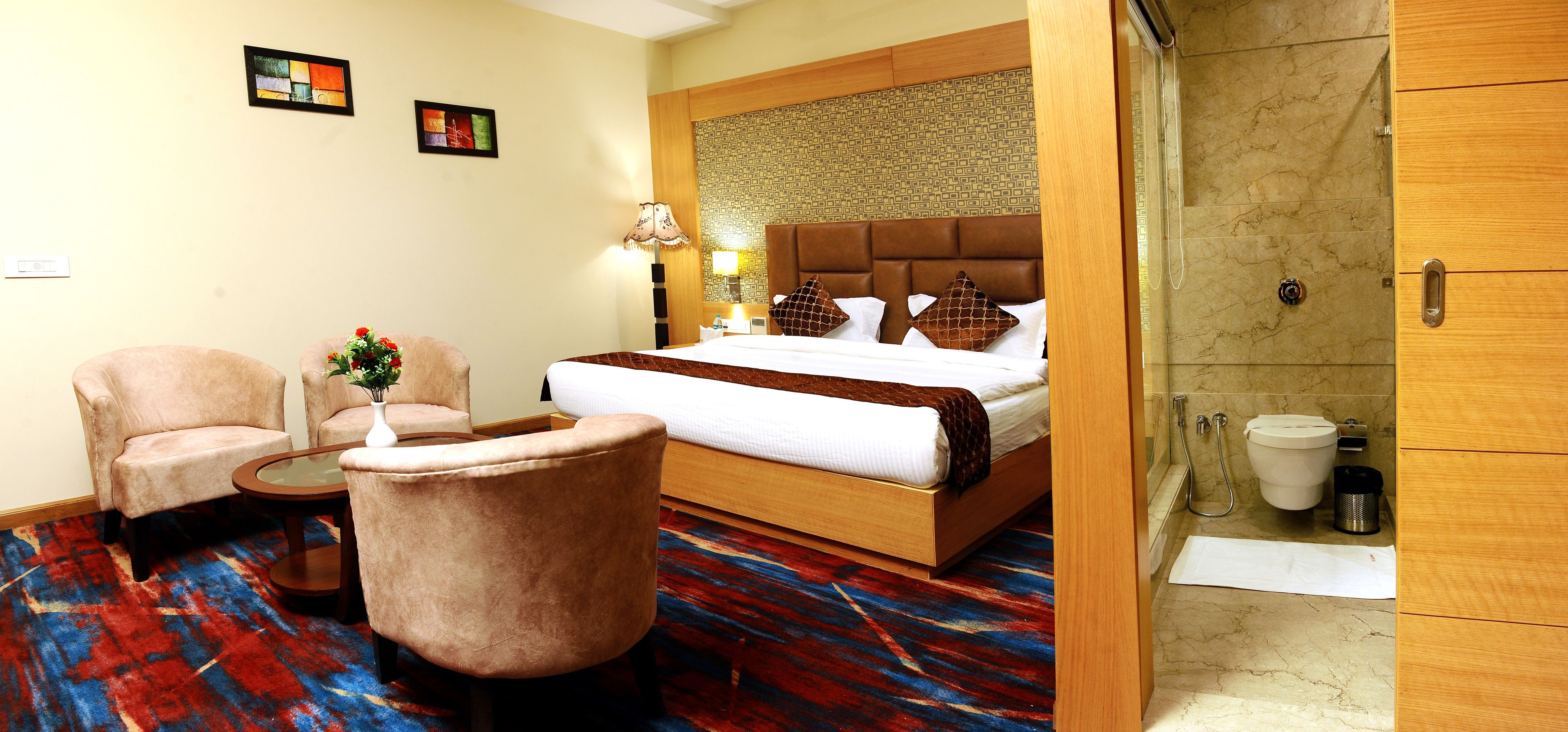 Habitación de hotel con cama, dos sillones, una mesita, un florero con flores y zona de ducha.