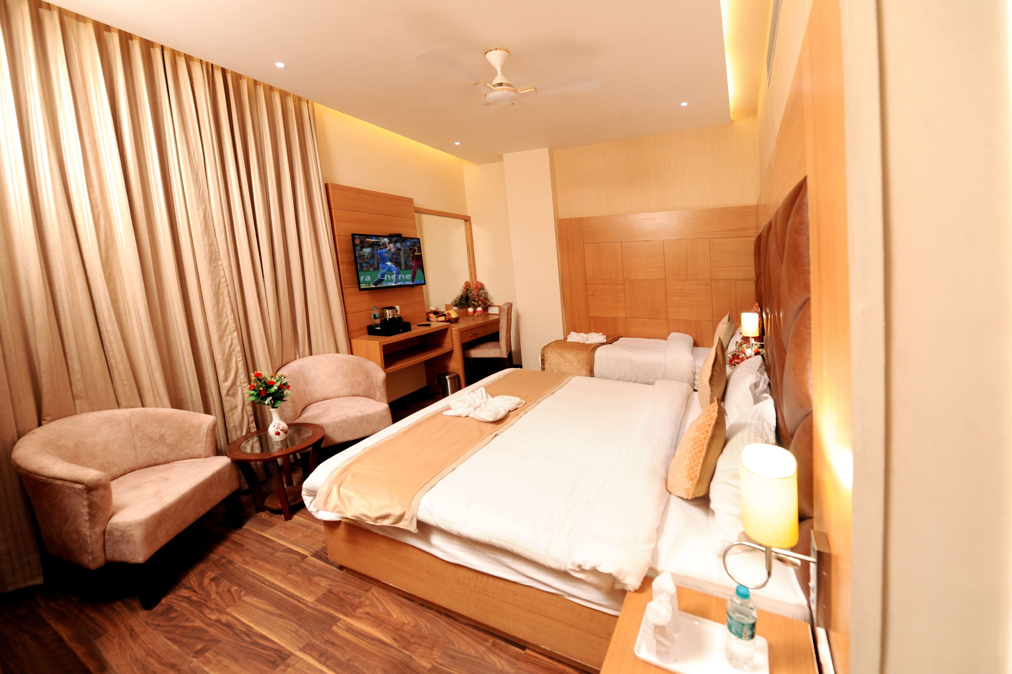 A hotel room with a bed, two armchairs, a desk, a television, and a ceiling fan.