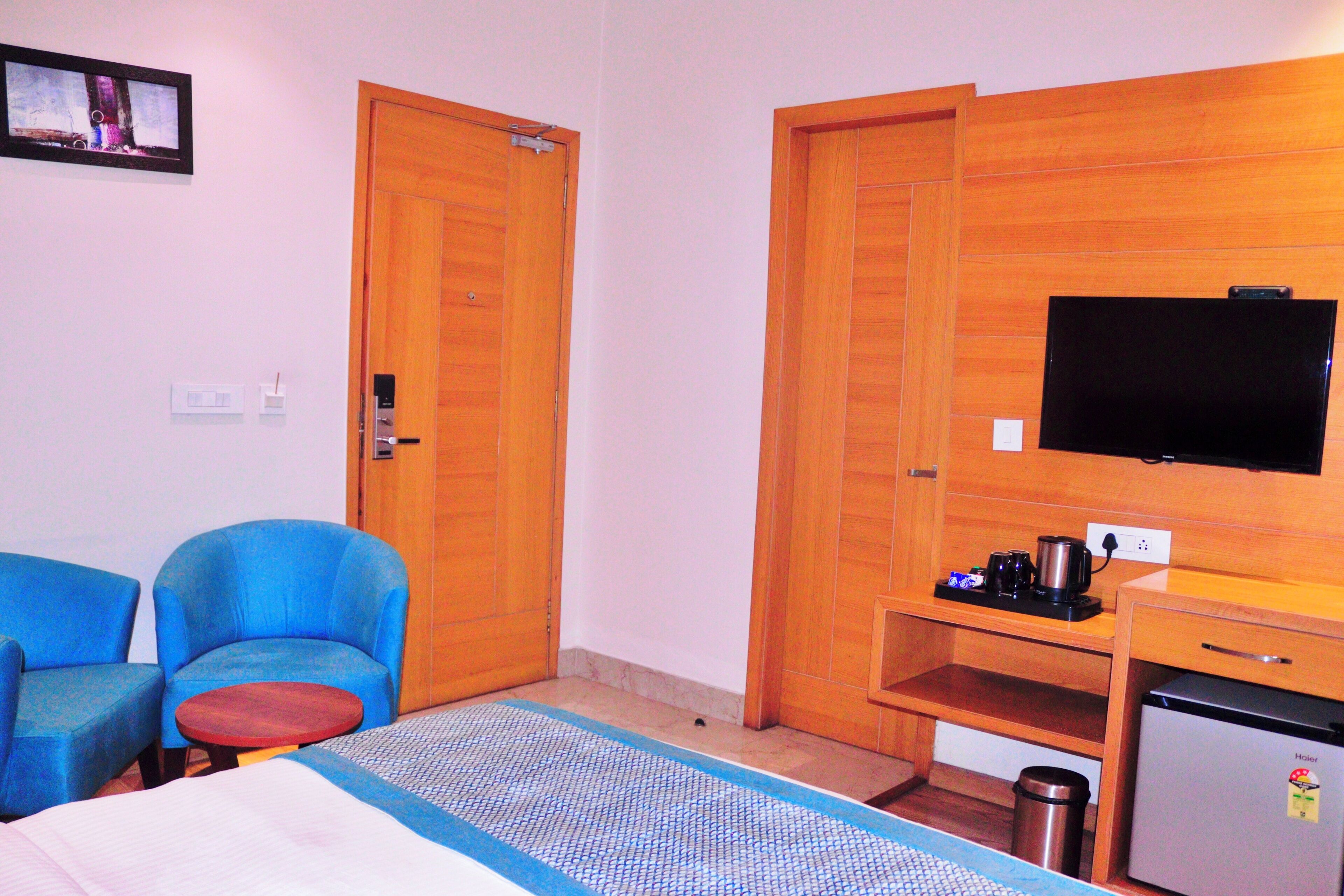 Camera d'albergo con un letto, due poltrone blu, un tavolino, una TV, un mini-frigo e armadi in legno.