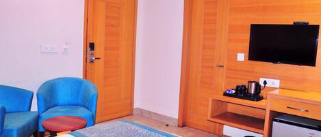 Camera d'albergo con un letto, due poltrone blu, un tavolino, una TV, un mini-frigo e armadi in legno.