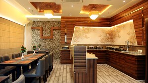 A modern kitchen with wooden cabinetry, a central island, and a dining area with a long table and chairs. - Hotel Landmark Near Golden Temple (Amritsar)