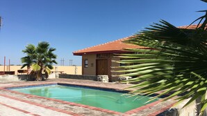 Una piscina con borde de azulejos, una palmera y un edificio con tejado de tejas rojas.