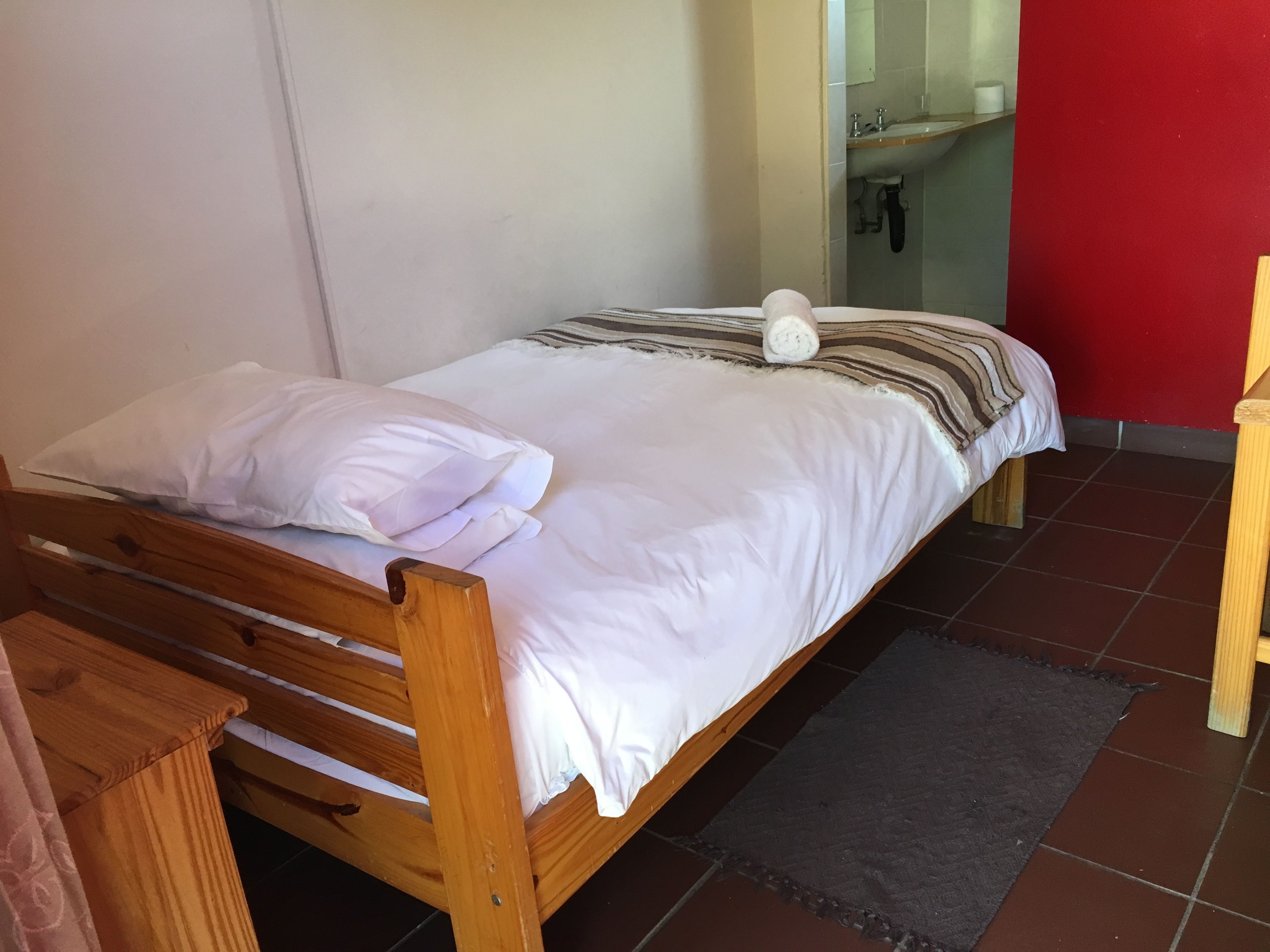 Una cama individual con ropa de cama blanca y una manta a rayas, un cabecero de madera y una mesita de noche pequeña.