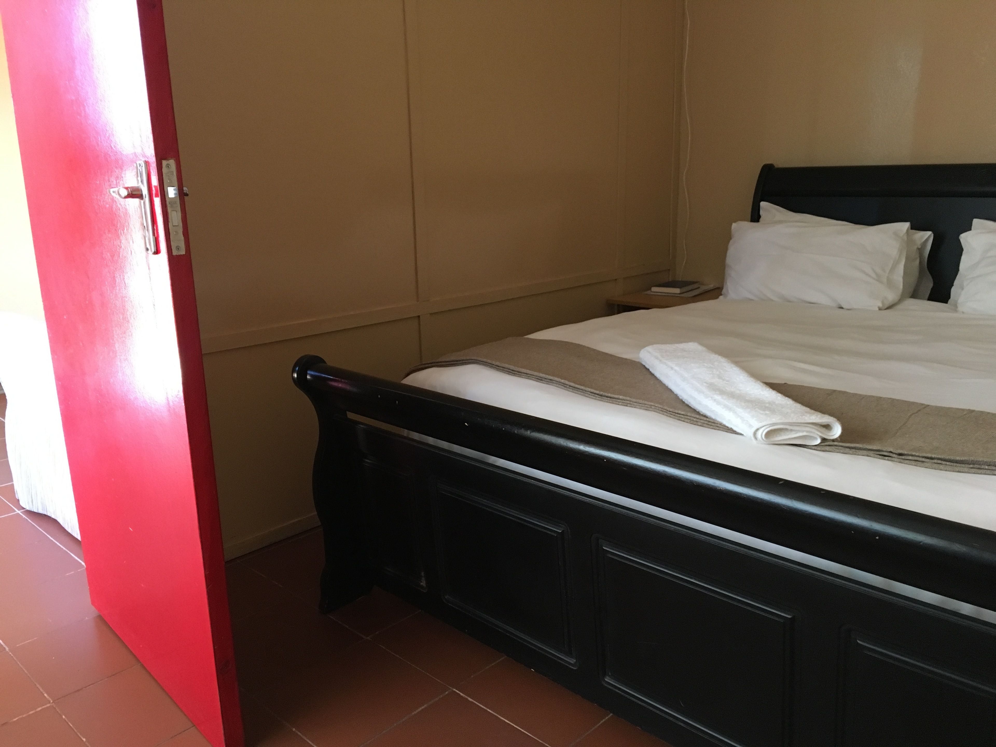 A hotel room with a bed, a red door, and a tiled floor.