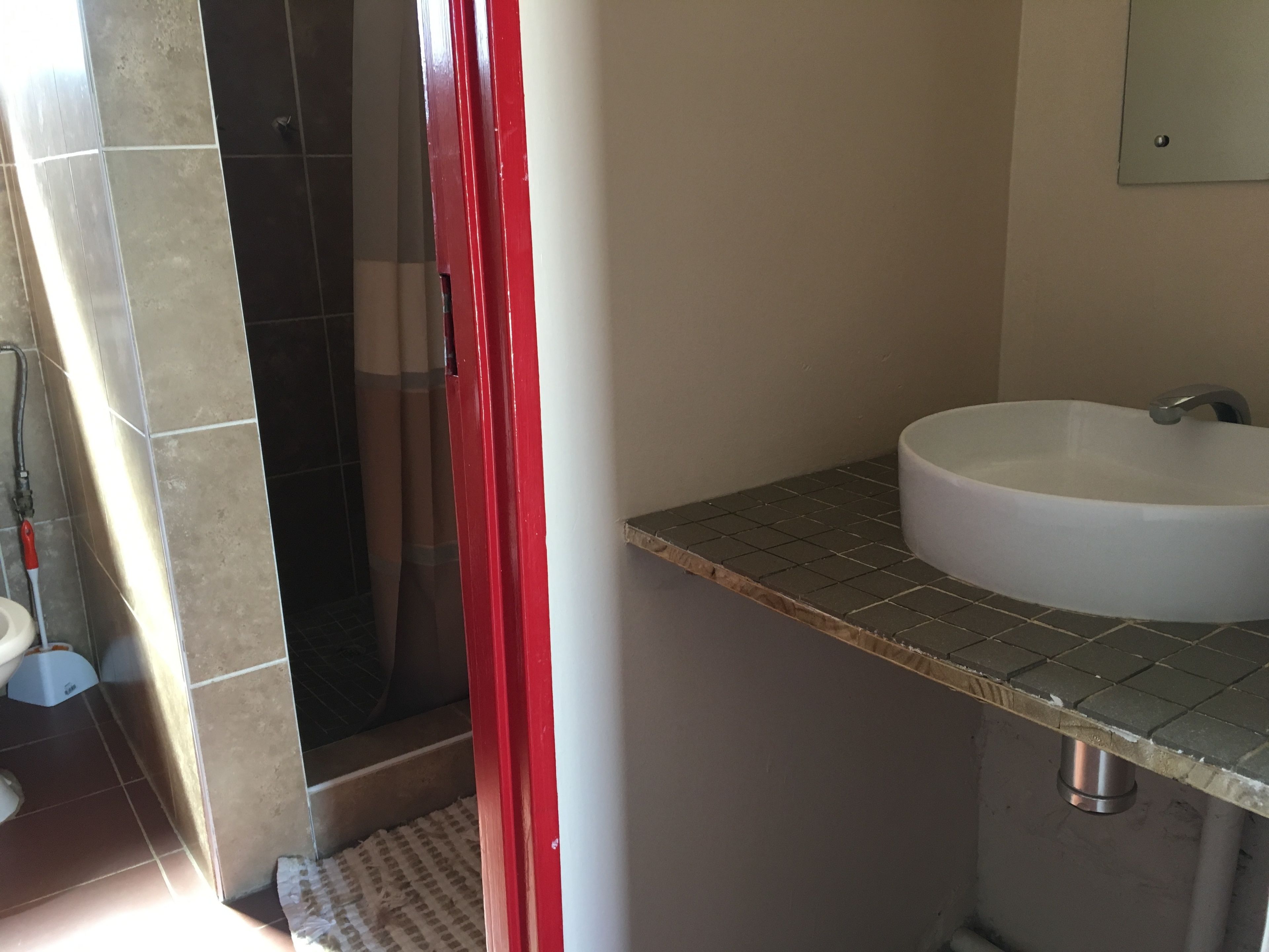 Une salle de bain avec un lavabo blanc, une douche et un rideau rouge.
