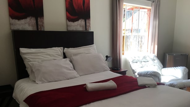 Una cama bien hecha con ropa de cama blanca y roja, un cabecero y una silla con estampado floral.