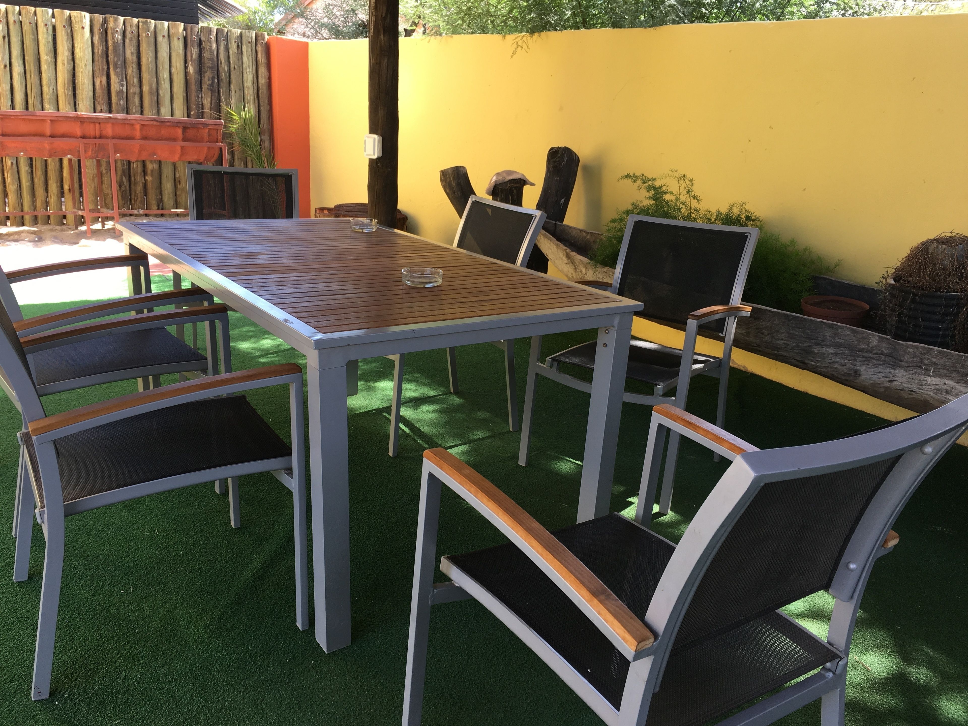 Un patio exterior con una mesa y sillas, rodeado por un muro amarillo y una valla de madera.