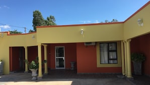 Un edificio con fachada amarilla, techo rojo y un patio empedrado.