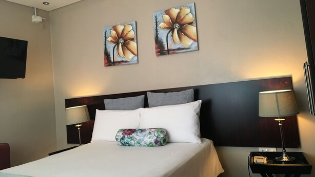 A hotel room with a bed, two wall-mounted paintings, a television, and a bedside lamp. - Yana Bed & Breakfast (Gaborone)