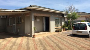 A building with a tiled roof, a paved entrance, and a parked white car. - Yana Bed & Breakfast (Gaborone)