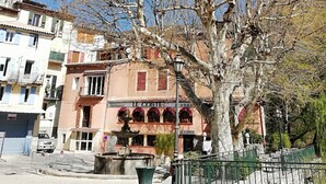 A tree-lined street with a restaurant named "LE COSTE" in the background. - - Large cozy studio ---- (Puget-Théniers)