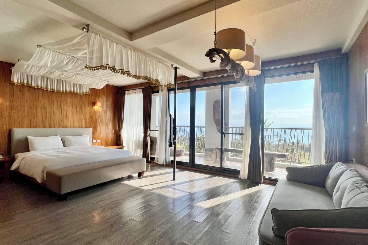 Un dormitorio amplio con una cama grande, un sofá y un balcón con vistas.