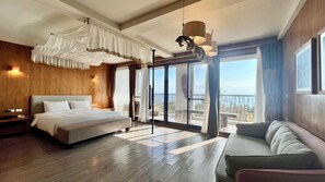 A spacious bedroom with a large bed, a sofa, and a balcony with a view.