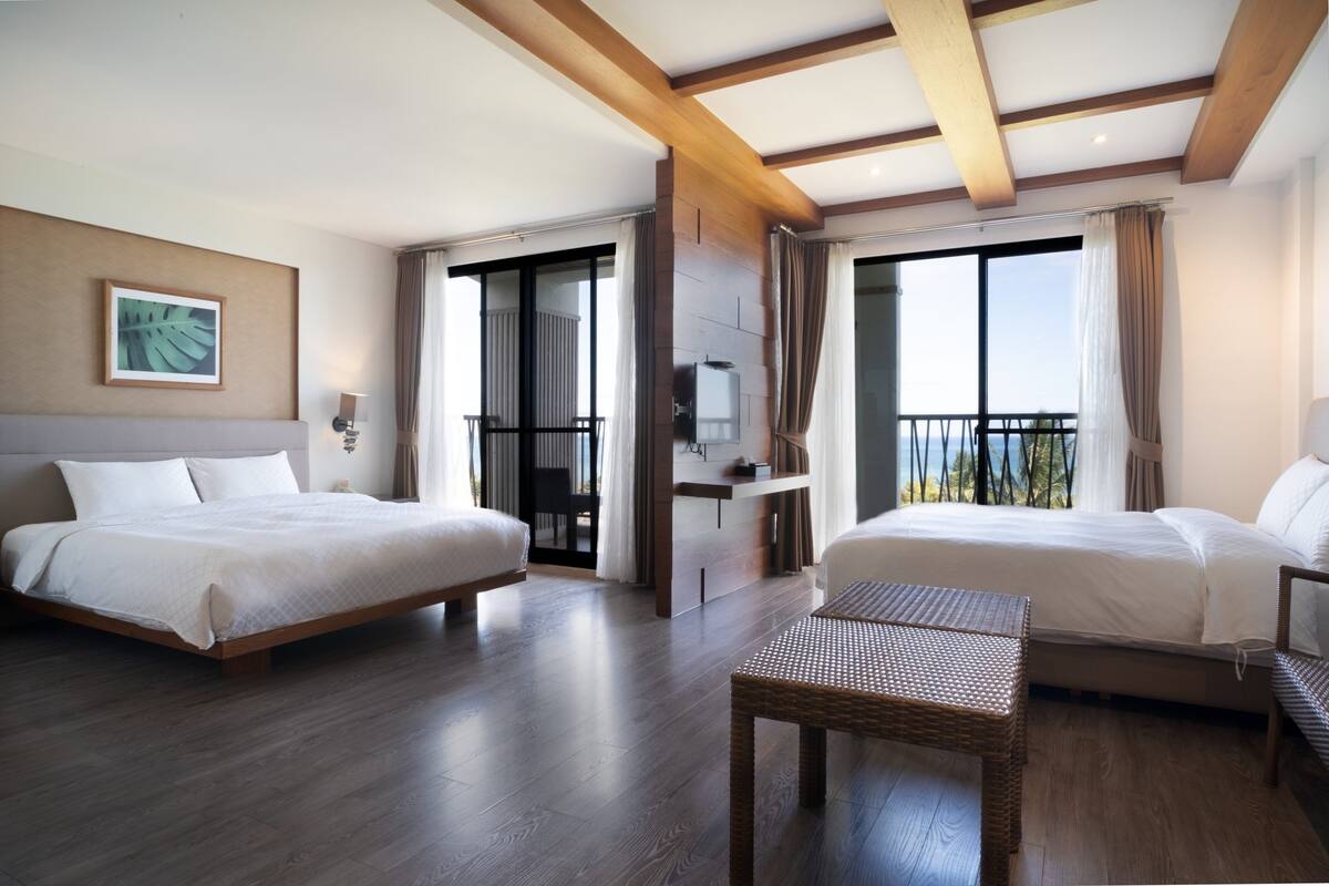 Habitación de hotel con dos camas, una mesita, un televisor y un balcón con cortinas.