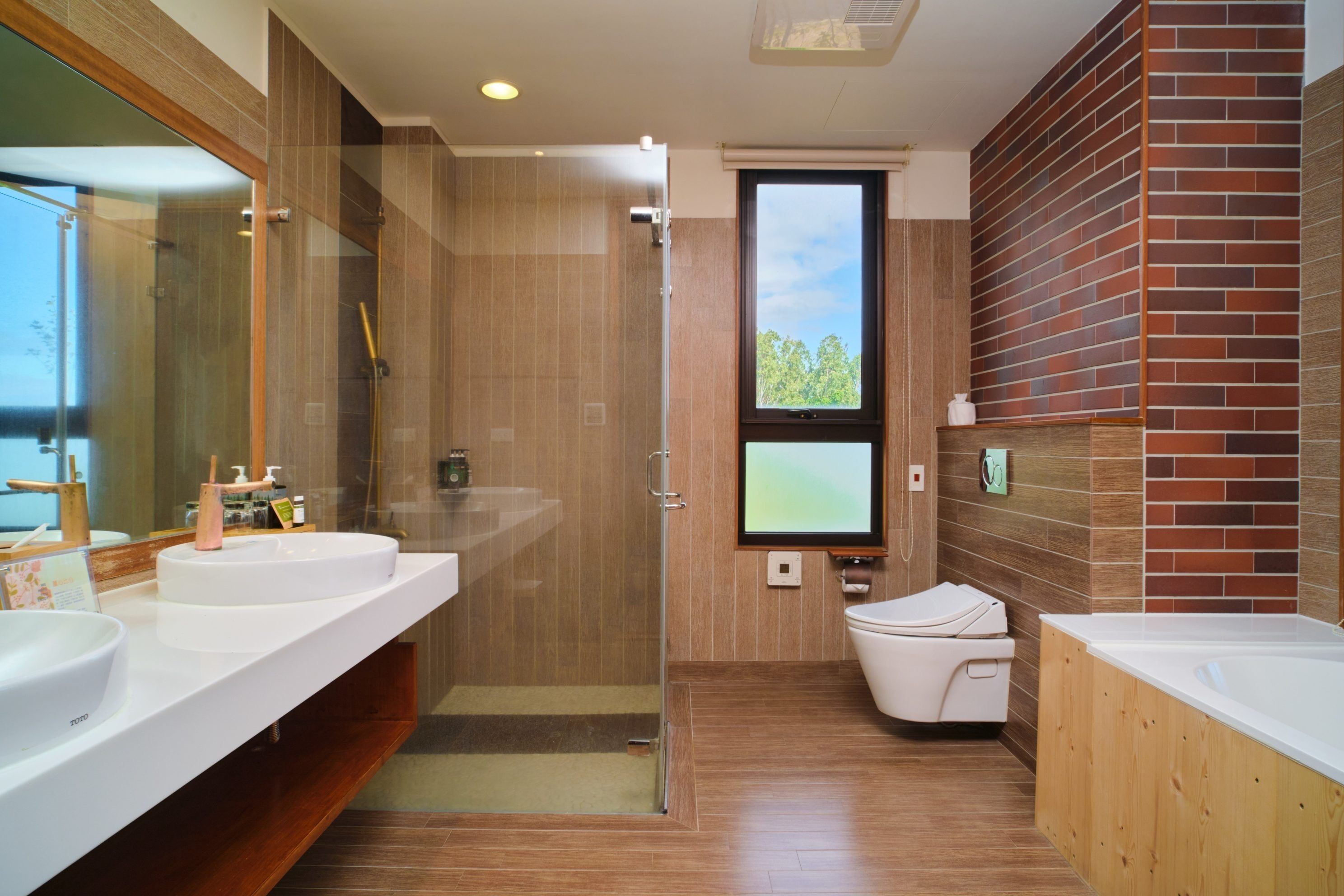 Un baño moderno con dos lavamanos, una cabina de ducha con mampara de vidrio, inodoro y un ventanal grande.