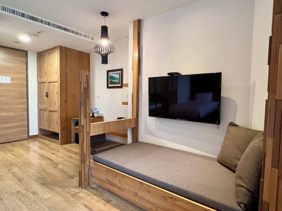 Una habitación moderna con suelo de madera, un banco empotrado con cojines, un televisor de pantalla plana montado en la pared y una mesita con un marco de fotos y algunos objetos encima.
