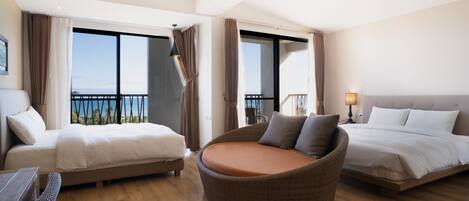 A hotel room with two beds, a wicker chair, and a view of the sea.