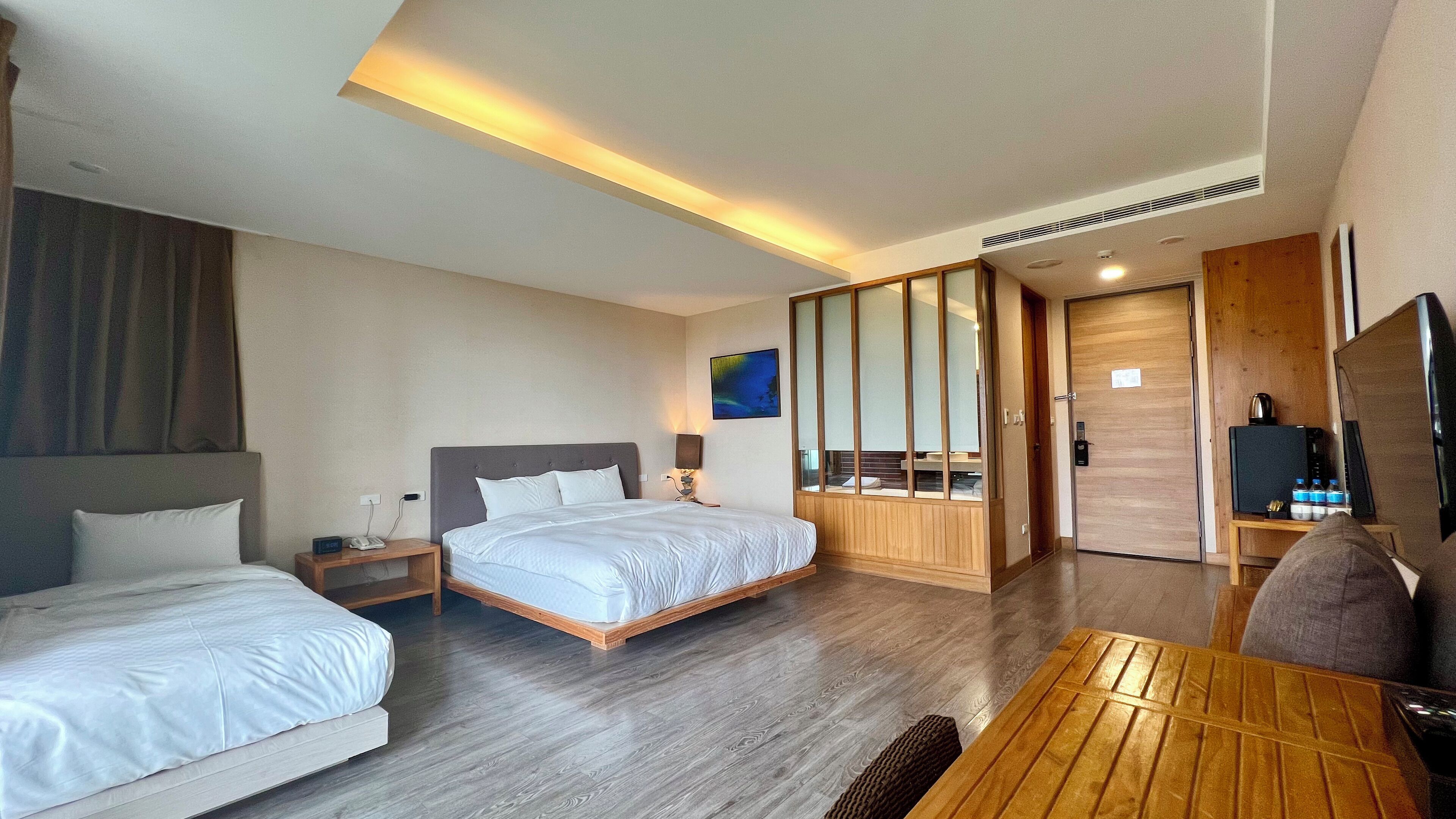 Habitación de hotel con dos camas, un escritorio de madera, un televisor y un espejo grande.