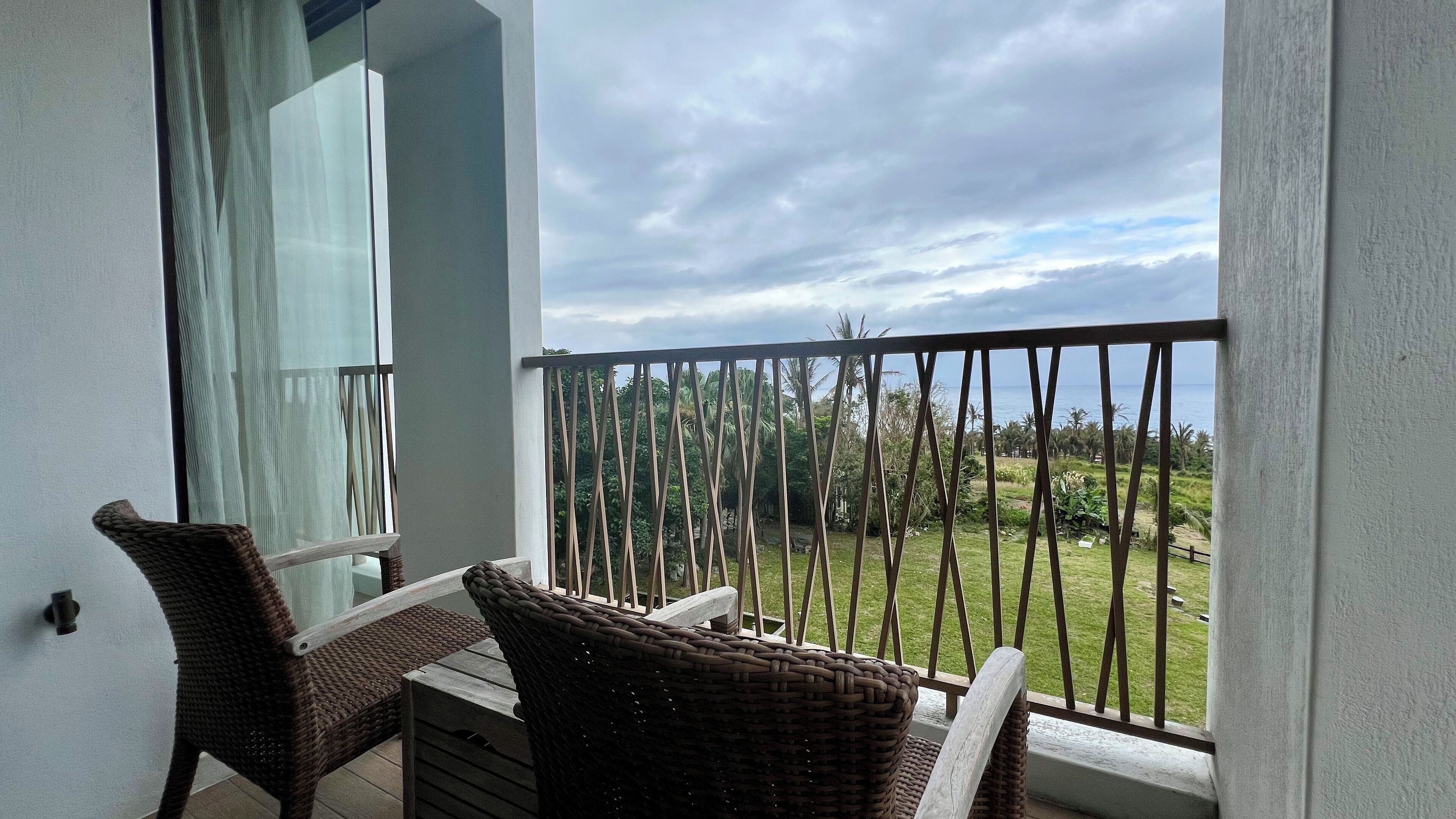 Un balcón con muebles de mimbre y vistas a un área verde con palmeras.