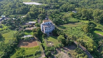 Vista aérea de un edificio grande de varios pisos rodeado de abundante vegetación y un pequeño estanque.