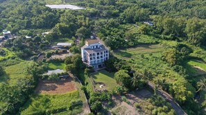 An aerial view of a large, multi-story building surrounded by lush greenery and a small pond.