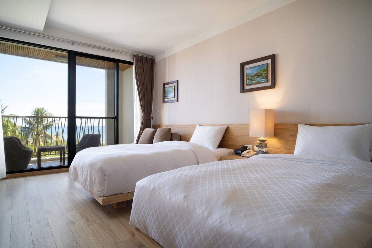 Habitación de hotel con dos camas, un balcón con vistas y un cuadro en la pared.