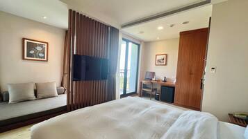 Habitación de hotel con una cama grande, un escritorio con computadora, un televisor y un balcón con cortinas.