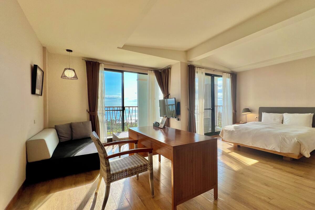 Habitación de hotel con cama, escritorio, sillón, sofá y balcón con vistas.