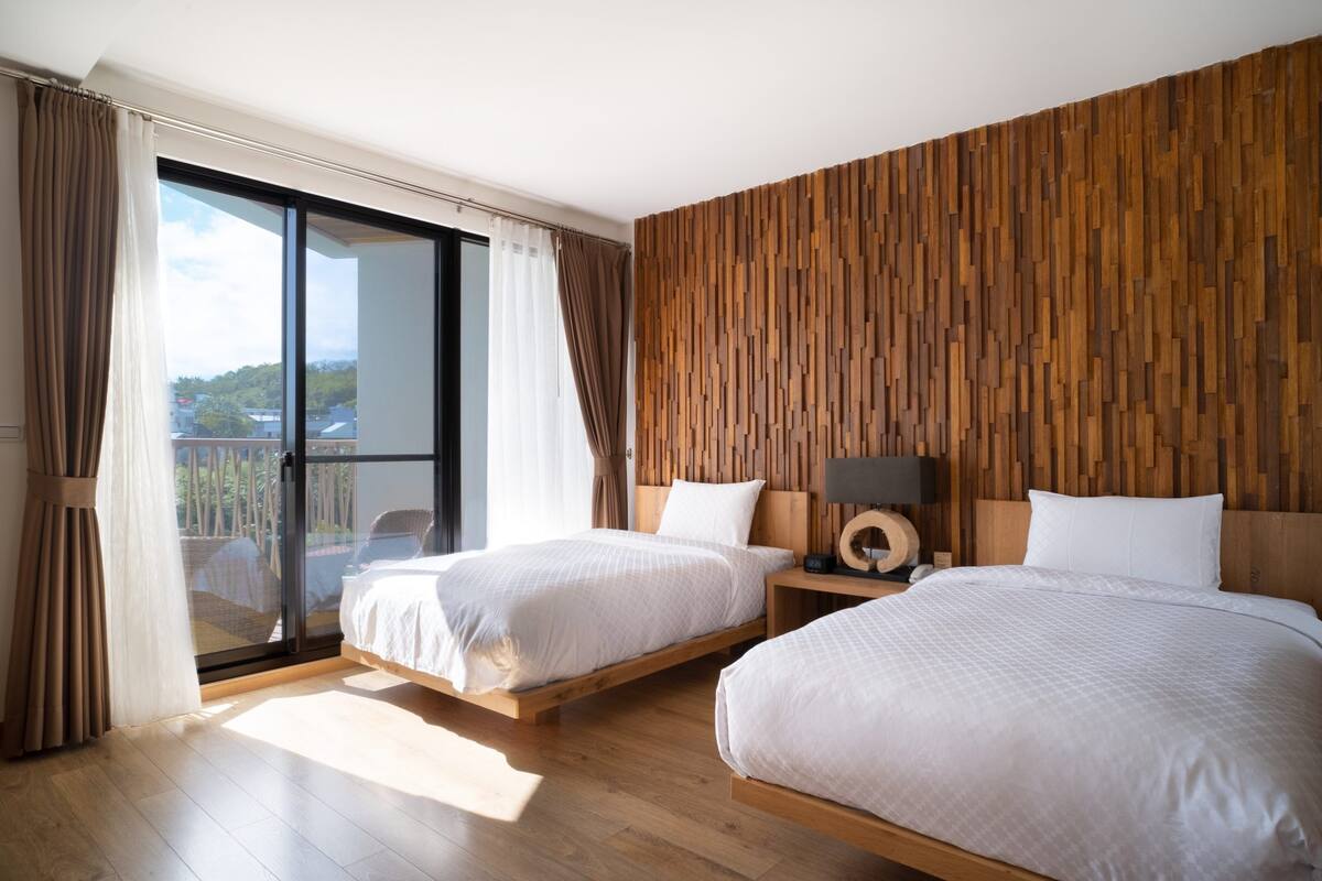Habitación de hotel con dos camas, un panel de pared de madera, un amplio ventanal corredero y vistas al exterior.