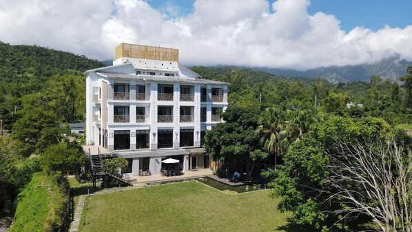 A multi-story building with a central courtyard, surrounded by lush greenery and mountains in the background.