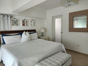 Une chambre bien rangée, avec un grand lit, une table de chevet avec une lampe et une porte.