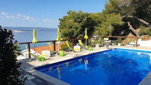 A swimming pool with a wooden deck, lounge chairs, and umbrellas. - Apartments Mistral (Omis)