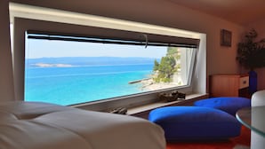 A room with a large window overlooking a coastal view, a wooden cabinet, and a potted plant. - Apartments Mistral (Omis)